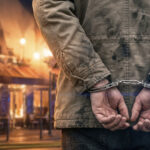 Арестованный человек и горящее кафе на заднем фоне